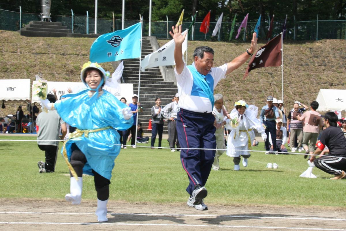 両手を上げ、最高の笑顔でゴールテープを切る町民