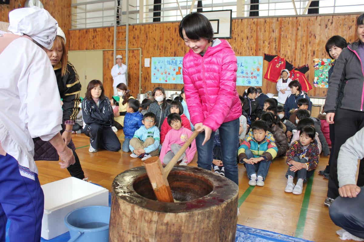 笑顔でもちつきする生徒と、見守るボランティアの方々