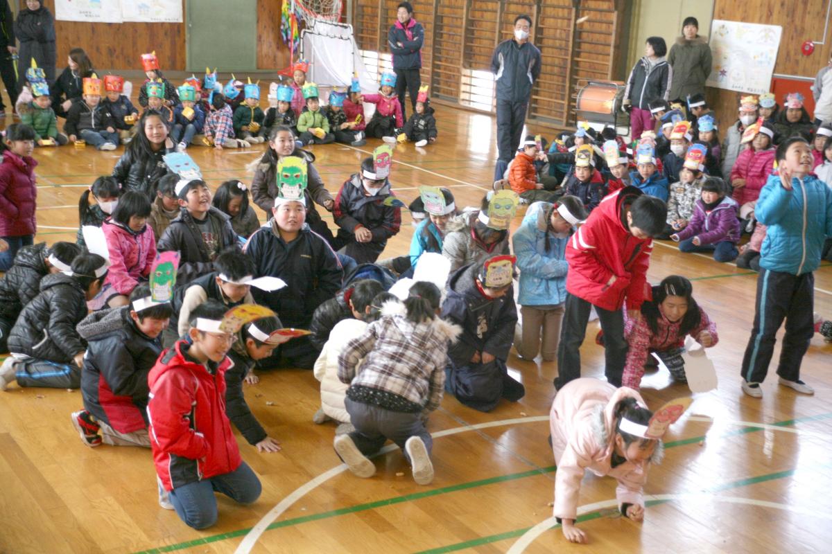 ステージの5年生たちから投げられた豆を拾う鬼のお面を付けた子どもたち