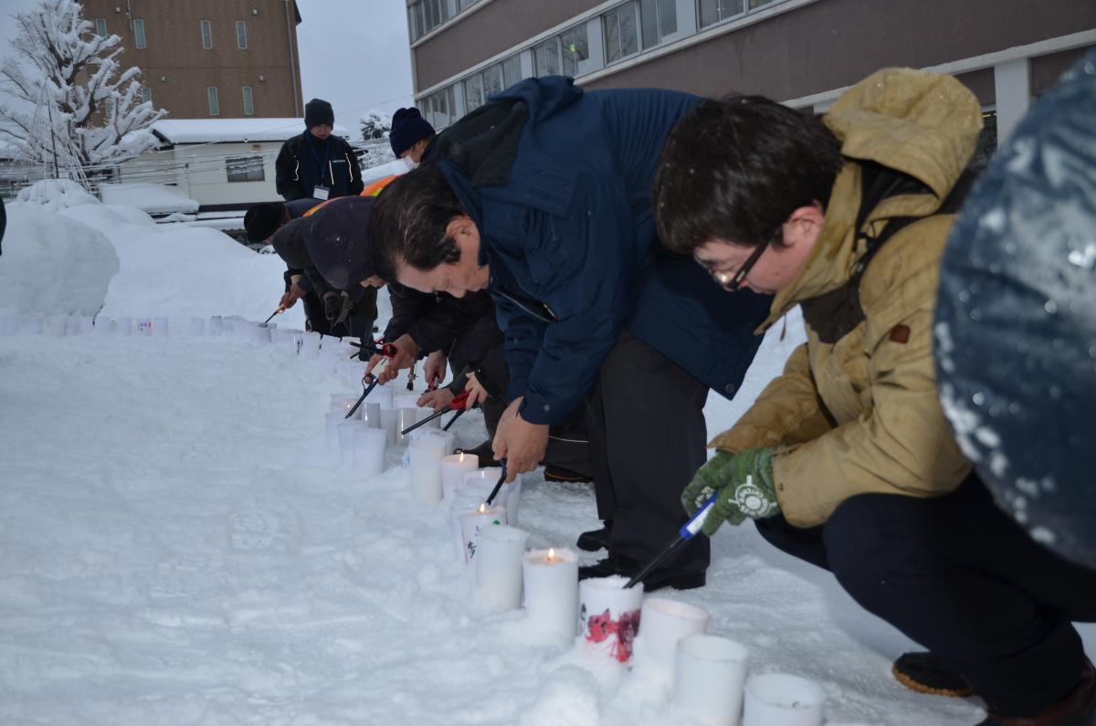 雪が積もり真っ白になった前庭に並べたろうそくに火を灯す参加者たち（2）