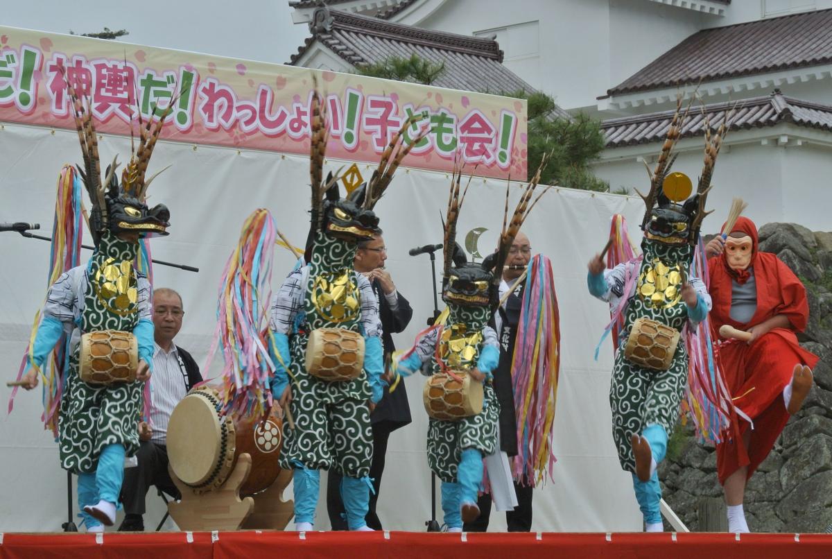 小雨が降る中、特設ステージに登場した鹿役の子ども4人と野猿、お囃子担当の保存会メンバー