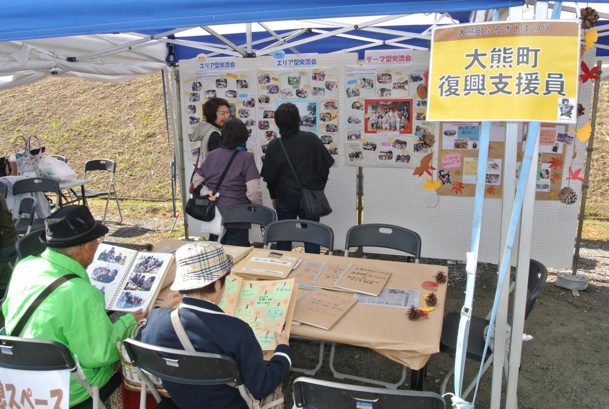 町復興支援員のブースに展示された町民交流会の写真を見る来場者