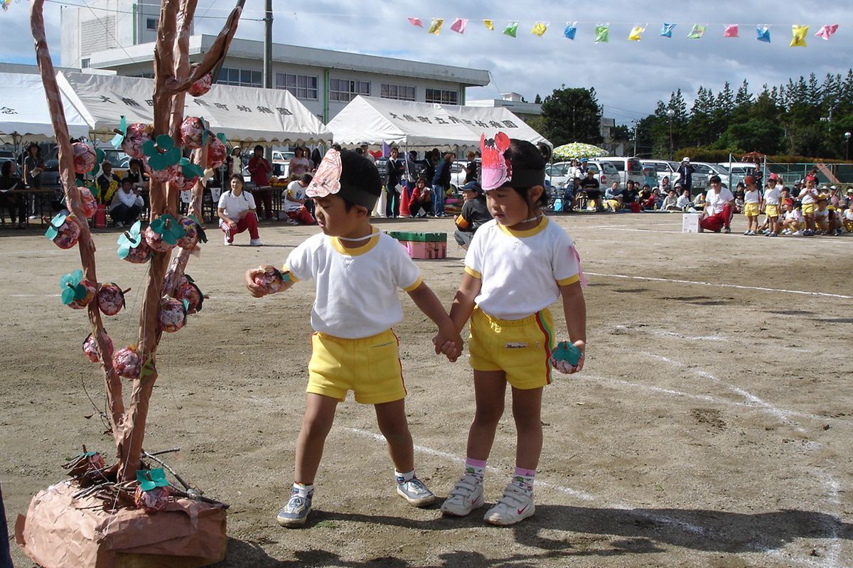 お友だちと手をつないで木に柿を付ける園児