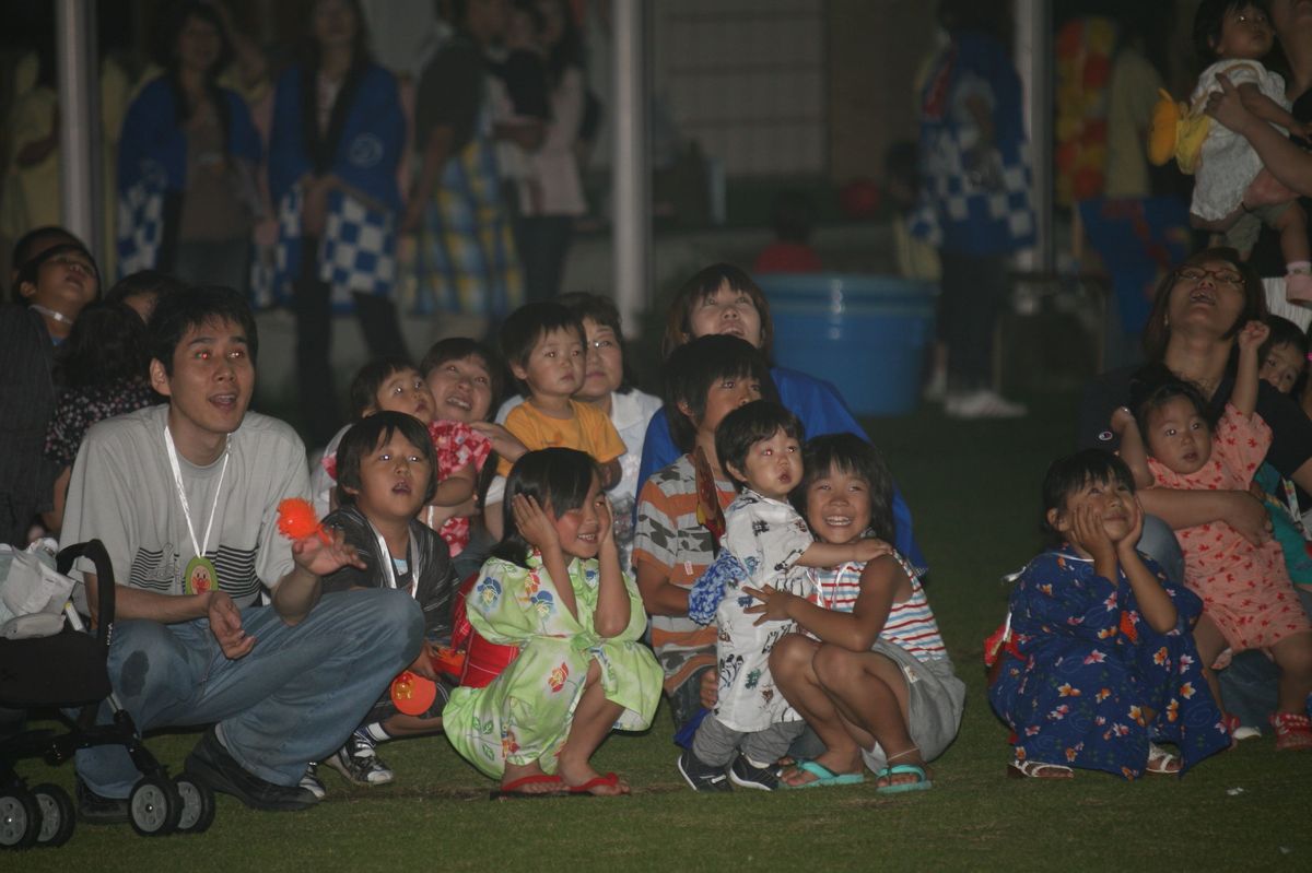 祭りの最後に行われた花火大会で空に咲く花火を見上げる子どもたちと保護者の方