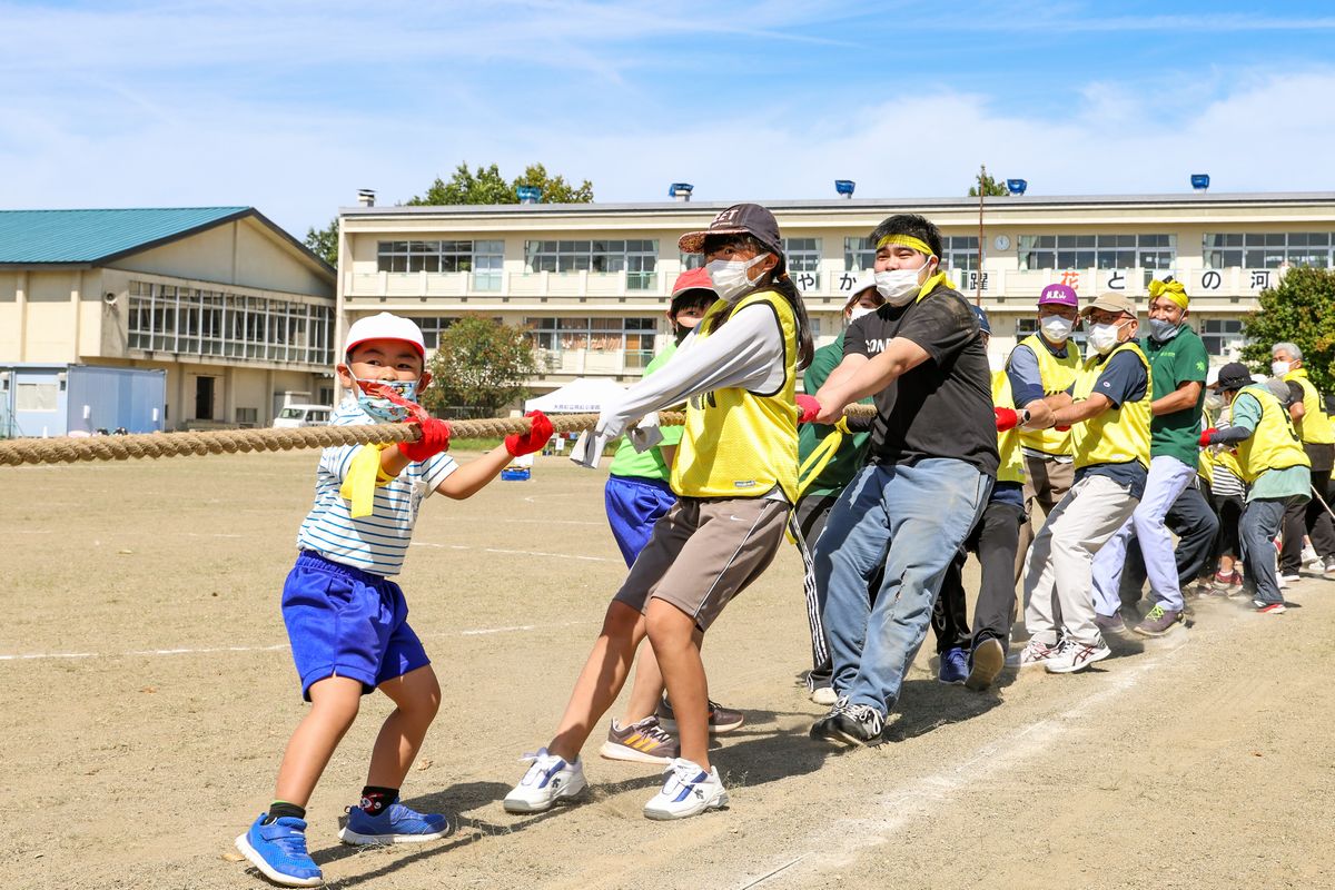 会津若松市の町立学び舎ゆめの森の校庭で9月17日、スポーツフェスティバルが開かれました。同校は来年度町内で再開する予定のため、会津若松市で運動会が行われるのは今回が最後。児童生徒や園児、卒業生や保護者、招待者、学生ボランティア、地域の皆さん約80人が集まり、最後の運動会を楽しみました。写真は、巨大鮭の絵が貼られたスクールバスをチームごとに引っ張りタイムを競う大熊のシャケにかけろ！です。