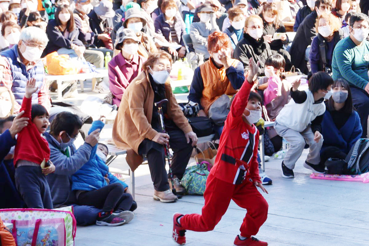 ステージでは、お笑い芸人のあばれる君、サンシャイン池崎さんのお笑いライブや演歌歌手の神野美伽さんによる歌謡ショー、暴太郎戦隊ドンブラザーズショーが開かれ、観客を大いに沸かせました。写真はステージ上に上がろうと元気よく手を上げアピールする子どもたちの様子。