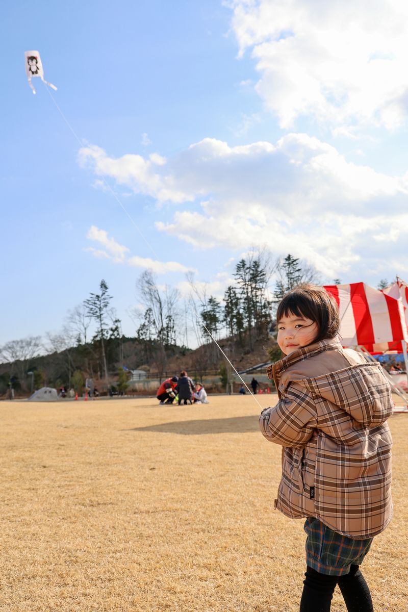 青空の下、高く上がったまあちゃんの凧揚げを楽しむ子ども。