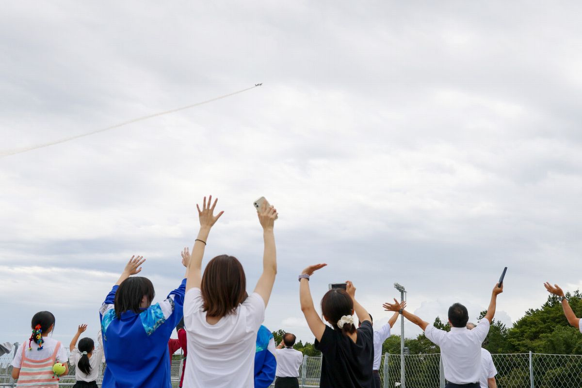 上空を飛ぶ室屋さんの飛行機に向かって手を振る児童生徒ら