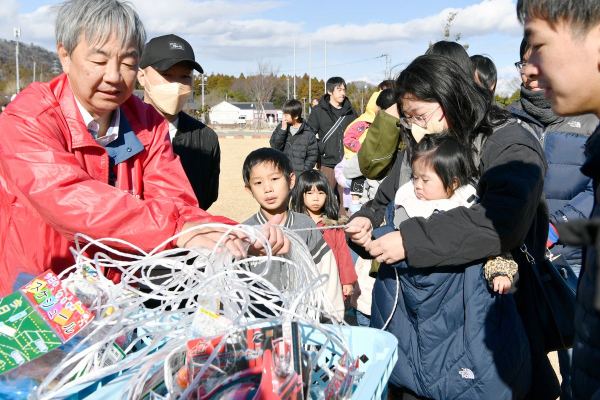 紐くじ（紐の先に景品がついていて、束ねた紐の中から1本引いて景品を当てるくじ引き）を楽しむ参加者。