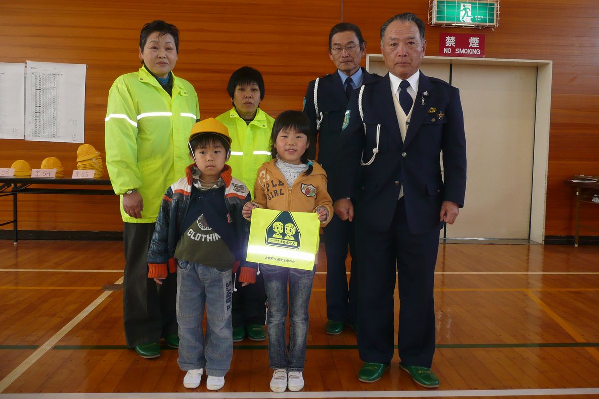 贈られた黄色い帽子とランドセルカバーを持ち笑顔で記念撮影する児童たち