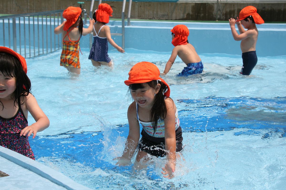 プールの中で水をすくって楽しむ園児