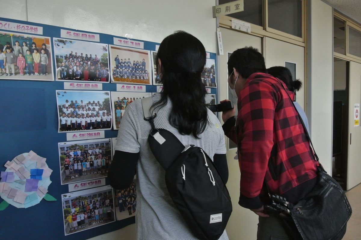 当時の全学年の記念写真を見つけカメラに収める家族