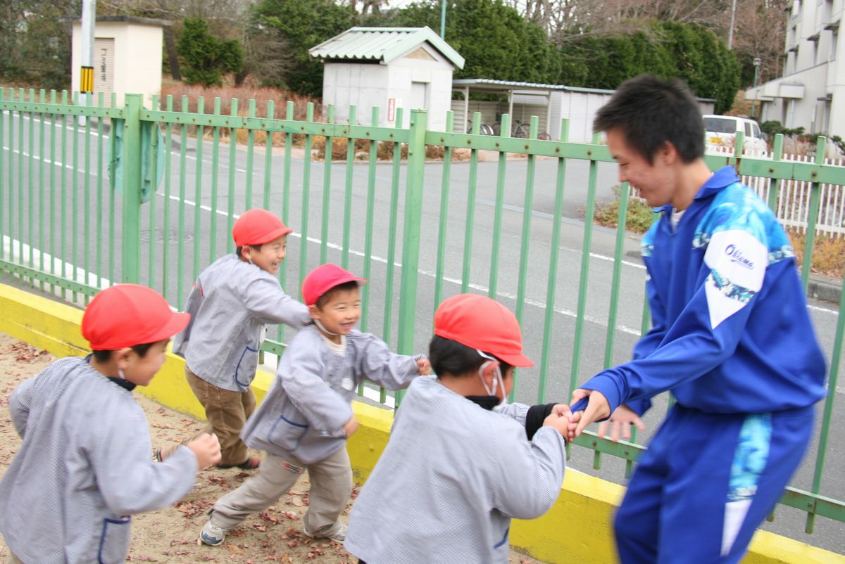 園庭で鬼ごっこをして遊ぶ園児と中学生