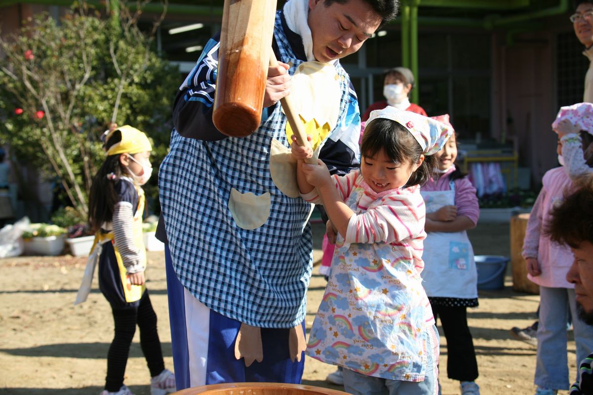 先生と一緒に杵を持ち、嬉しそうに餅をつく園児（2）