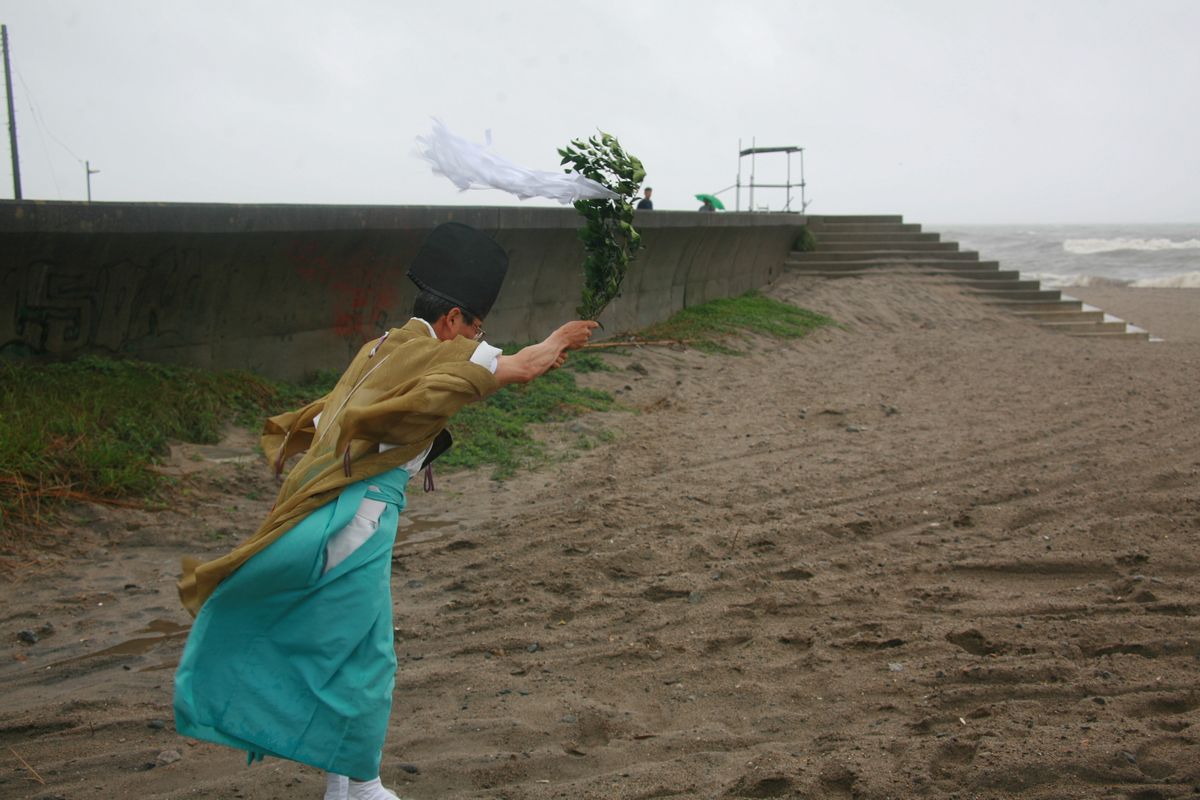 台風4号が急接近し風が吹き荒れる中、海に向かい安全祈願をする神官