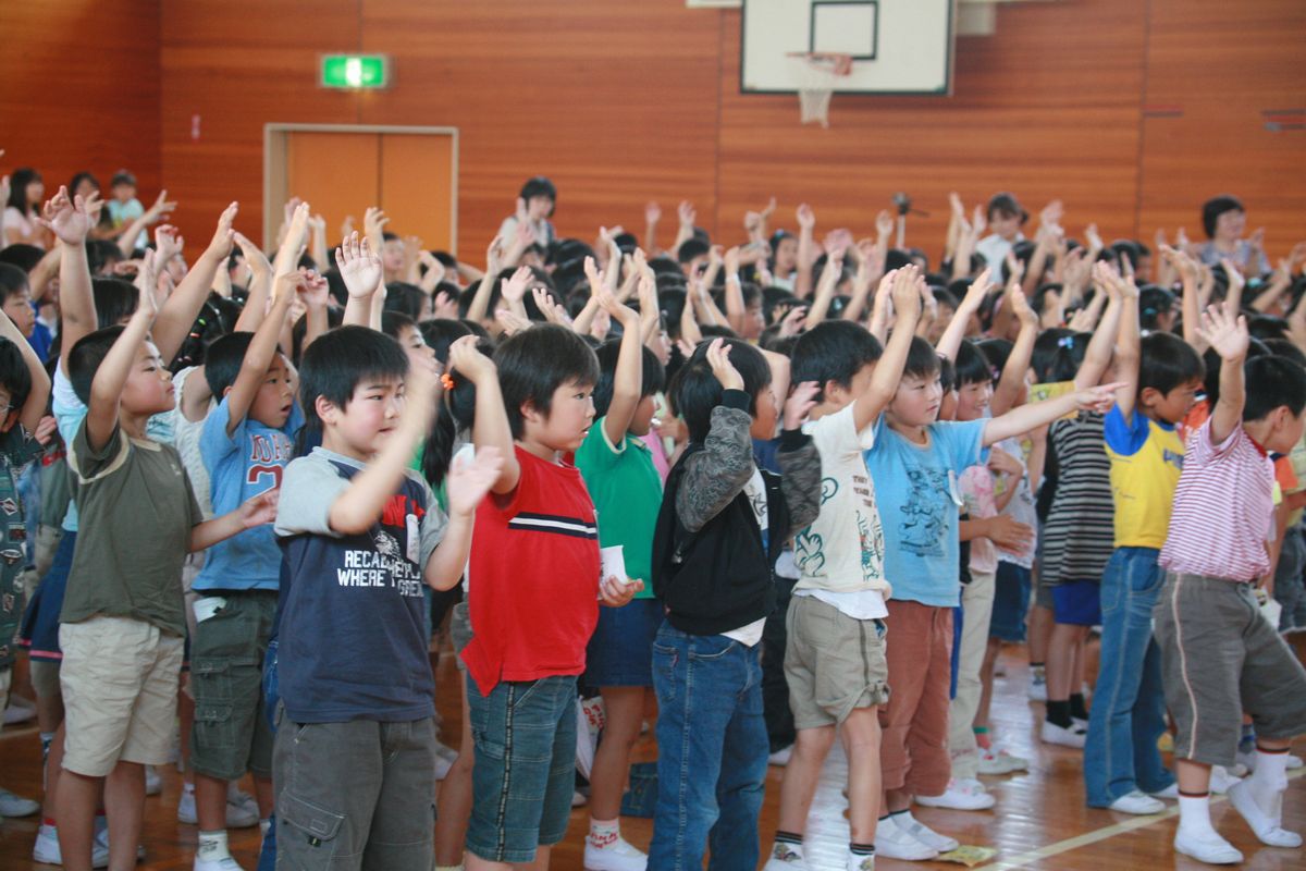 ステージの人形と一緒に手を上げて踊る児童たち