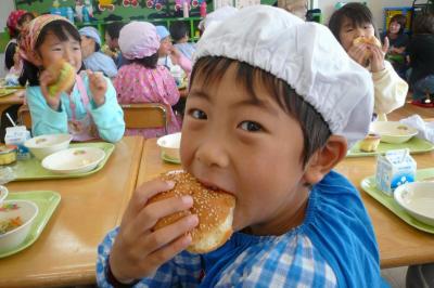 給食のハンバーガーを大きな口を開けて頬張る園児